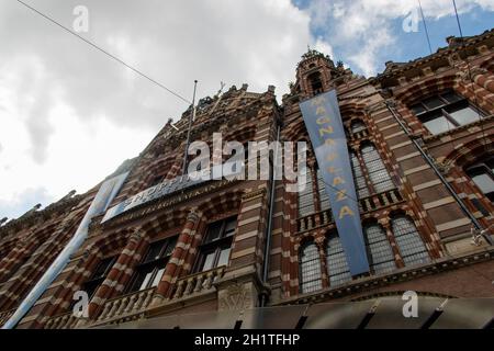 Erstaunliche Low-Angle-Ansicht der ehemaligen Amsterdam Hauptpost unter leicht bewölktem Himmel. Wunderschönes europäisches Gebäude mit neugotischer Architektur Stockfoto