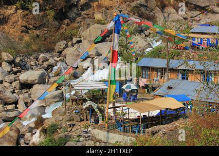 Szene auf dem Weg nach Langtang, Nepal. Fluss und kleine Hütten. Bunten Gebetsfahnen. Stockfoto