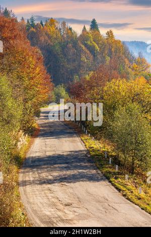 Alte Bergstraße im Morgenlicht. Bäume in farbenfrohem Laub entlang der Serpentine. Erkunden Sie das Konzept der Landschaft Stockfoto