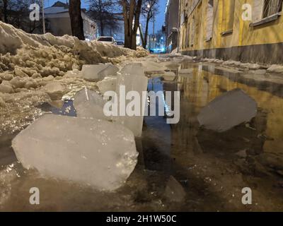 Das Eis fiel vom Dach auf dem Bürgersteig, die Spiegelung von Häusern im Wasser. Stockfoto