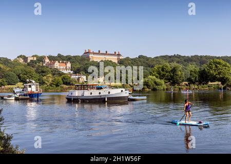 Ein Paddelboarder fährt auf der Themse in Meadowside, East Twickenham, mit dem Petersham Hotel und den Royal Star & Garter Home Buildings dahinter. Stockfoto