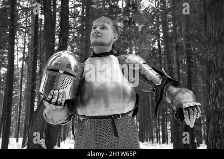Ritter in Rüstung und mit einem Schwert mitten in einem Winterwald. Klassische Militäruniform. Stockfoto
