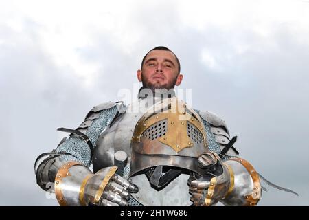 Ritter in Rüstung auf dem Hintergrund einer bewölkten Himmel. Ritterlichen Rüstung und Waffe. Semi-antik Foto. Stockfoto