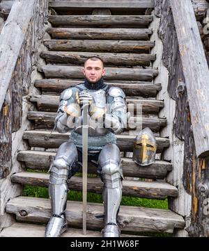 Ritter in der Rüstung auf die hölzerne Treppe. Ritterlichen Rüstung und Waffe. Semi-antik Foto. Stockfoto