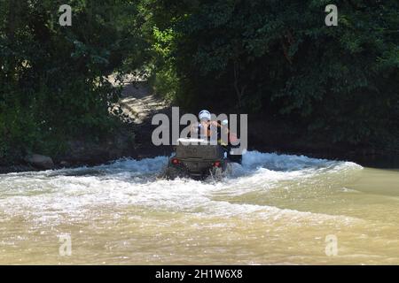 Der Mann auf dem ATV kreuzt einen Stream. Touristischen Spaziergänge auf einem cross-country Gelände. Stockfoto