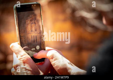 Tourist, der ein Foto mit einem Smartphone oder Handy der Schatzkammer aus dem Blickwinkel in Petra, in der Nähe von Wadi Musa, Jordanien, macht Stockfoto