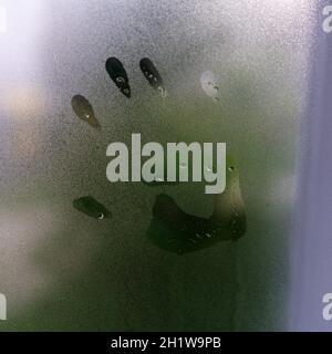 Kleiner Kinderhanddruck auf einem nebligen regnerischen Glas. Stockfoto