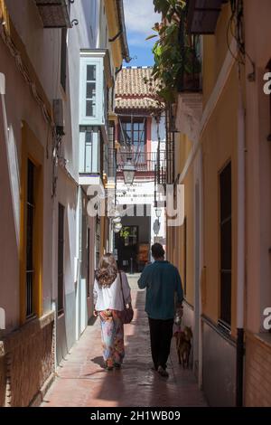 Ein touristisches Paar, das durch die enge Straße des Santa Cruz Viertels, dem historischen Viertel von Sevilla, Spanien, läuft Stockfoto