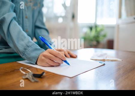 Welttag des Mietvertrags. Eine Frau signiert Dokumente, Schlüssel liegen auf dem Tisch. Nahaufnahme der Hände. Mieten und kaufen. Stockfoto