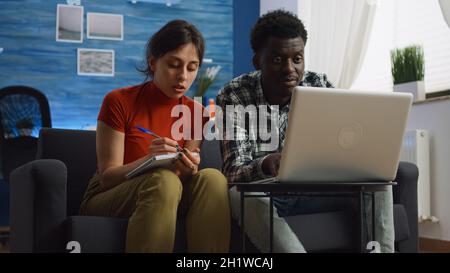 Junges interrassisches Paar, das Steuern und Papierkram mit Laptop und Notebook im Wohnzimmer berechnet. Ehemann und Ehefrau aus gemischter Rasse überprüfen Rechnungen und planen das Budget für Steuerzahlungen zu Hause Stockfoto