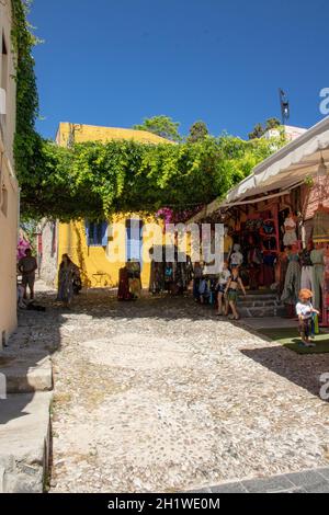 RHODOS, Griechenland - 07. JUNI 2021. Eine Seitenstraße der berühmten Sokrates Street in der Altstadt von Rhodos mit einem Gelben Haus und einem Bekleidungsgeschäft. Stockfoto