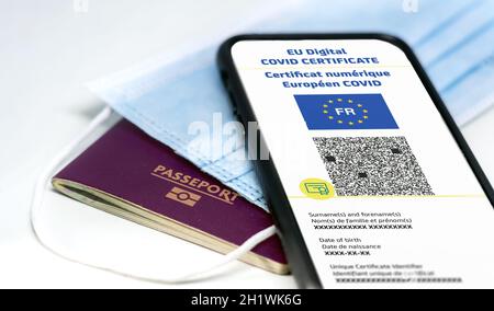 Französisches EU Digital COVID Zertifikat mit dem QR-Code auf dem Bildschirm eines Mobiltelefons über einer OP-Maske und einem französischen Pass. Immunität gegen Covid-1 Stockfoto