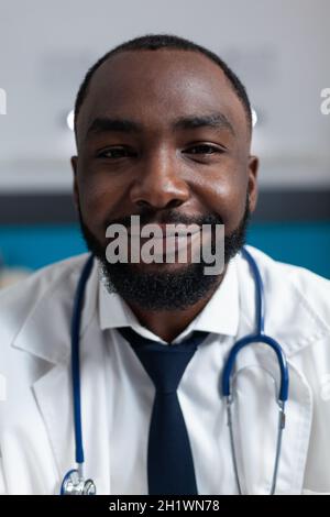 Nahaufnahme eines afroamerikanischen Therapeuten-Arztes mit Stethoskop, der in die Kamera schaut, während er im Krankenhausbüro arbeitet. Praktizierender Mann, der den Bericht über pharmazeutische Verschreibungen analysiert Stockfoto
