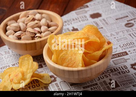 Pistazien und Kartoffelchips in Holzschüsseln auf Bastelpapier. Snacks bis Bier Stockfoto