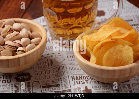 Ein Becher kaltes Bier mit Pistazien-Nüssen und Kartoffelchips in Holzschüsseln. Stockfoto