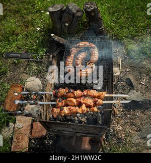 Mann, der Schaschlik oder Schischkebab über Holzkohle vorbereitet. Grillen Sie Fleisch und Würstchen oder Bratwurst auf einem Grillrost im Hinterhof. Gegrilltes Fleisch auf Metallspieß Stockfoto