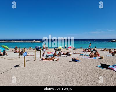 Monte-Carlo, Monaco - 1. August 2021: Menschenmenge, Die Im Sommer Am Strand Von Larvotto Sonnenbaden, Blaues Mittelmeer In Monte-Carlo, Monaco Auf Der Fre Stockfoto