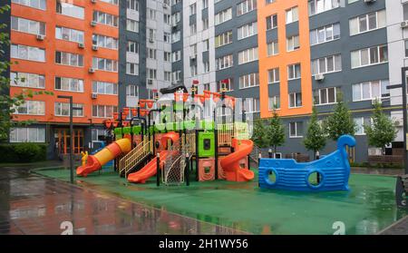Ein Innenhof aus Hochhäusern mit einem neuen, modernen, farbenfrohen und großen Spielplatz an einem regnerischen Sommertag ohne Menschen. Leerer Spielplatz im Freien. A p Stockfoto