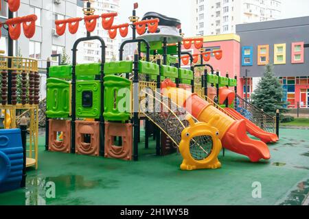 Ein Innenhof aus Hochhäusern mit einem neuen, modernen, farbenfrohen und großen Spielplatz an einem regnerischen Sommertag ohne Menschen. Leerer Spielplatz im Freien. A p Stockfoto