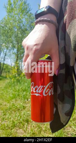 Hand hält eine Dose Coca Cola. Die Getränke werden vom amerikanischen Getränkekonzern The Coca-Cola Company hergestellt. Junge Frau mit Coca-Cola-Outdoo Stockfoto