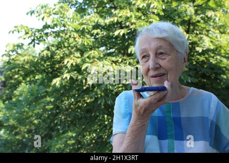 Charmante ältere Frau in rechteckiger, schwarz umrandter Brille mit Spracherkennungsfunktion auf dem Handy. Moderne ältere weibliche Holding elektronische gad Stockfoto