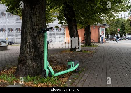 Riga, Lettland. 2021. August. Ein Elektroroller, der sich auf dem Bürgersteig einer Straße im Stadtzentrum an einen Baum lehnt Stockfoto