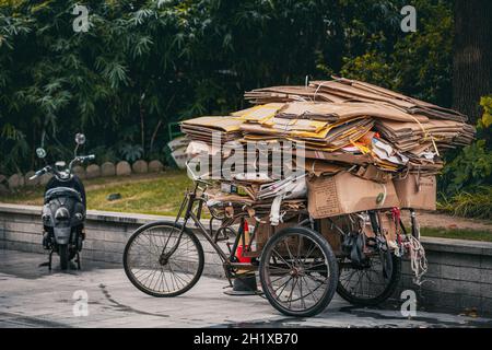 Hangzhou, China - 12. November 2019: Fahrrad mit Papierabfall auf dem Bürgersteig geparkt. Arme Chinesen helfen dem Staat, Müll zu recyceln. Stockfoto