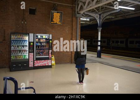 Doncaster, Großbritannien, 22. Mai 2021: Eine junge Frau mit Mantel, Rock und Handtasche wartet nachts am Bahnhof von doncaster Stockfoto