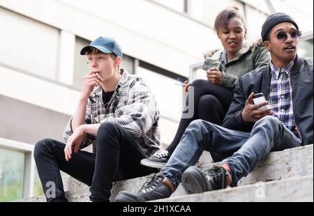 Eine Gruppe von trendigen jungen Freunden, die auf einer Treppe rauchen Stockfoto