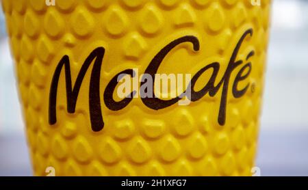 Gelbes Glas aus Papier mit Kaffee für McCafe-Drinks auf dem Tisch gegen die verschwommene Stadt von McDonald's. Hintergrund des Fast-Food-Geschäfts. Fastfood-Res Stockfoto