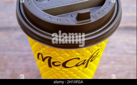 Gelbes Glas aus Papier mit Kaffee für McCafe-Drinks auf dem Tisch gegen die verschwommene Stadt von McDonald's. Hintergrund des Fast-Food-Geschäfts. Fastfood-Res Stockfoto