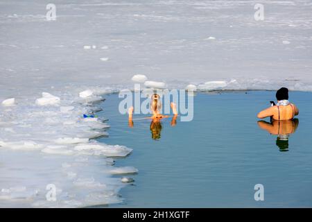 Krakau, Polen - 20. Februar 2021 : zwei junge Frauen tauchten in kaltem Wasser, während sie im Winter in einem Eisloch eines gefrorenen Kryspinow-Sees schwammen Stockfoto