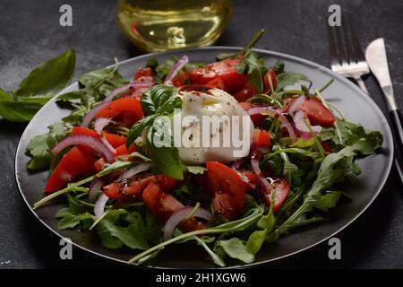 Salat mit Tomaten und Burrata-Käse mit Basilikum und Olivenöl auf dunklem Hintergrund. Traditionelles italienisches Gericht Burrata-Käse. Burrata serviert mit tomat Stockfoto