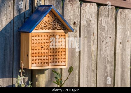 Ein Bienenhotel oder Insektenhotel in Form eines Hauses mit einem blau gestrichenen Dach, das an einem Holzzaun hängt Stockfoto