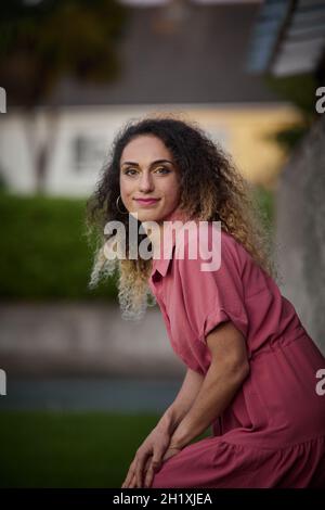 Preise blonde Frau mit lockigem Haar sitzt auf dem Stamm eines Baumes in schönen rosa Pin-up-Kleid. Stockfoto