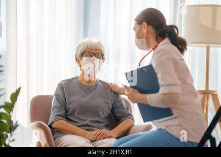 Arzt und ältere Frau mit Gesichtsmasken während des Coronavirus- und Grippeausbruchs. Virenschutz. COVID-2019. Masken übernehmen. Stockfoto