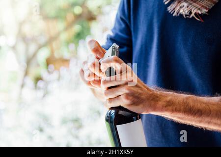 Ein junger Mann, der eine Flasche Rotwein mit einem Korkenzieher öffnet. Asado-Tag in Argentinien. Stockfoto