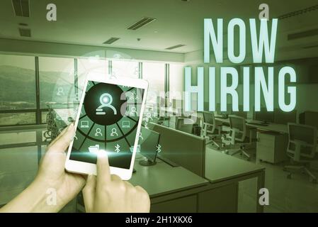 Textschild zeigt Now Hiring, Word geschrieben über die Suche Bewertung der Arbeitsbeziehung mit zukünftigen Mitarbeitern Hand berühren Bildschirm von Handy Showi Stockfoto