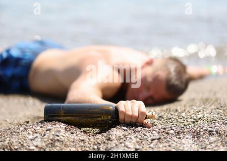 Betrunkener männlicher Tourist liegt am Strand mit einer Flasche Wein Stockfoto