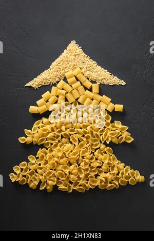 Alternative kreative Weihnachtsbaum von verschiedenen trockenen Pasta auf schwarzem Hintergrund. Weihnachtskarte. Blick von oben. Konzept für Essens- und Urlaubsreise. Stockfoto