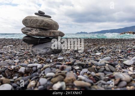 Steinpyramide am Strand gegen raues Meer. Auf dem Backgorund dem Vorgebirge von Portofino (Italien). Konzept der Spiritualität, entspannen, zen. Stockfoto