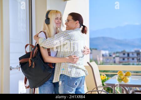 Mama umarmte ihre Tochter im Teenageralter auf der Veranda des Hauses nahe der Eingangstür und trifft Auf Wiedersehen. Stockfoto