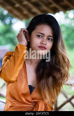 Wunderschöne javanische Hündin in einem orangefarbenen Kleid, die in einer Open-Air-Hütte sitzt. Stockfoto