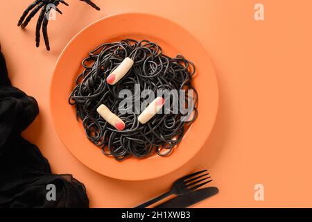 Halloween kreative italienische schwarze Pasta (Tintenfisch Tinte) verziert lustige Finger in Teller auf orangefarbenem Hintergrund. Blick von oben. Lebensmittelkonzept. Stockfoto