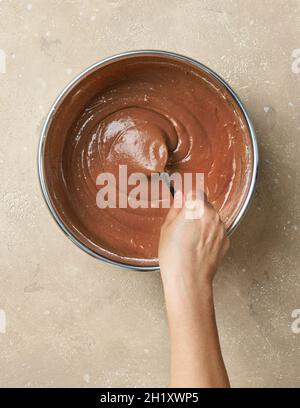 Prozess der Herstellung von Teig für Schokoladenkuchen. Mischen von Kakaopulver in Metallschüssel mit Teig auf Küchentisch, Draufsicht Stockfoto