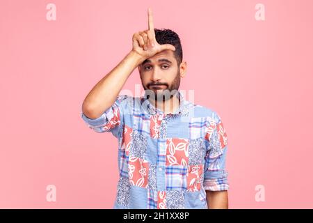 Deprimierter Mann mit Bart in blauem Casual-Style-Hemd, der die Hand an der Stirn hält und mit den Fingern eine lockere Geste zeigt, Probleme hat, sieht unglücklich aus. Innenaufnahme des Studios isoliert auf rosa Hintergrund. Stockfoto