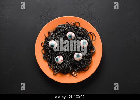 Halloween lustige italienische schwarze Pasta Tintenfisch Tinte verziert Horror Augen in orange Platte mit Rauchtrank auf schwarzem Hintergrund. Horror-Essen für Party. Anzeigen Stockfoto