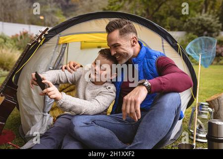 Kaukasischer Vater und Sohn machen ein Selfie, während sie in einem Zelt im Garten sitzen Stockfoto
