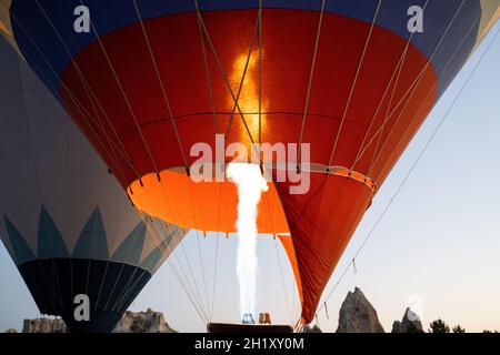 Vorderansicht Nahaufnahme des roten Heißluftballons, der vor dem Start auf dem Boden steht, mit Brennerflamme, die die Luft erwärmt Stockfoto