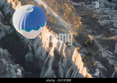 Draufsicht Nahaufnahme eines einsamen Heißluftballons mit blau-weißen Farbmustern, die im Morgenlicht über das Panorama des Kappadokischen Tals aufsteigen Stockfoto